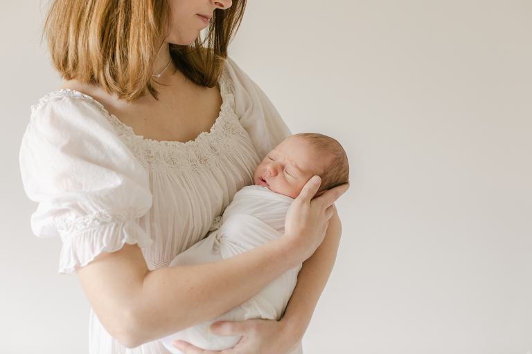 Mother cradling her newborn baby in a delicate white dress for a blog post about Birmingham Breastfeeding