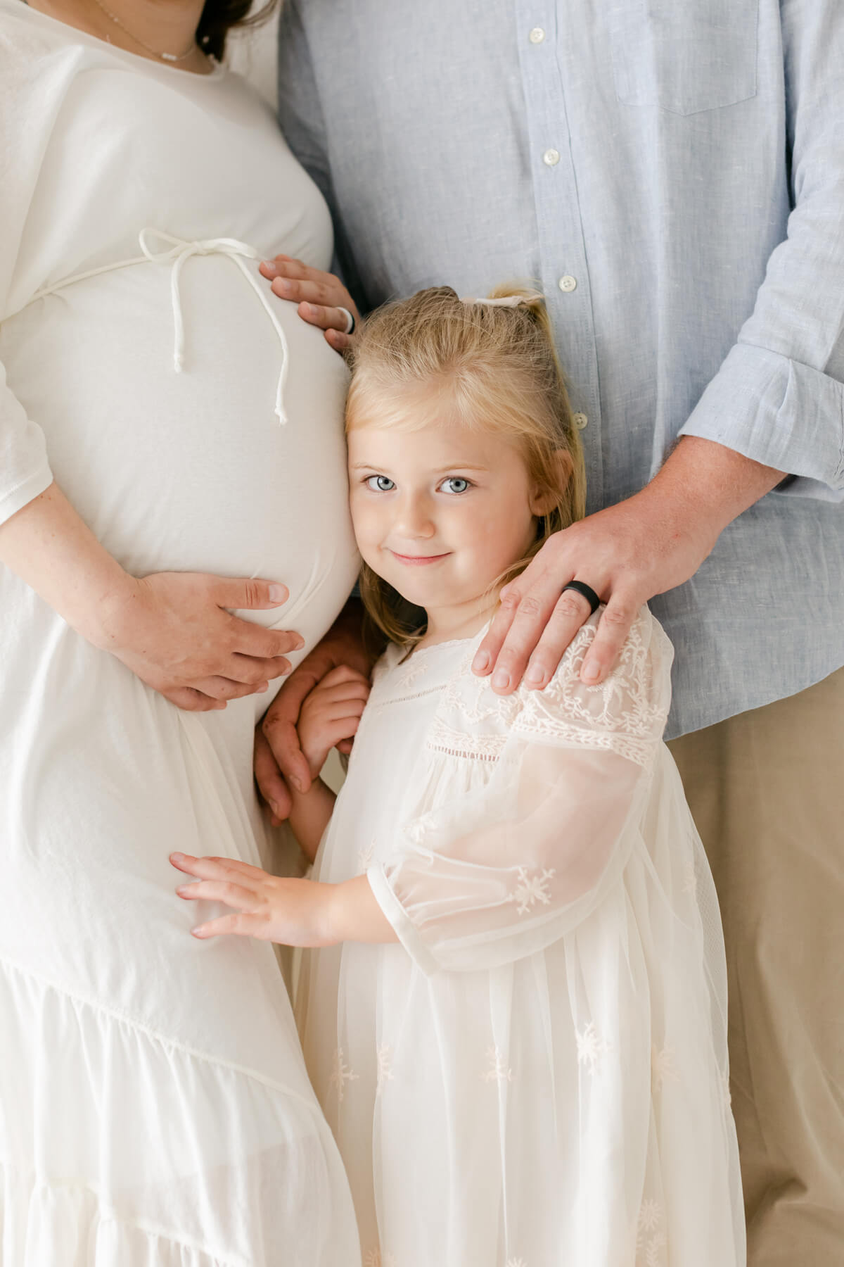sweet big sister smiles at the camera in maternity and family photographer Virginia Schultz's bright studio