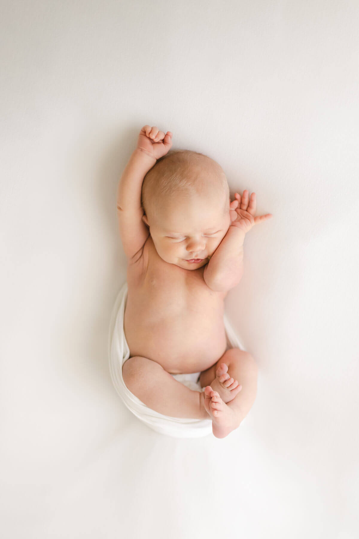 newborn stretches on a white blanket in omaha nebraska photographer Virginia Schultz studio