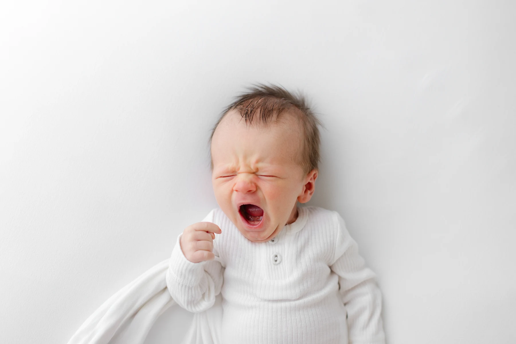 Newborn baby yawning while swaddled on a white backdrop during a studio session in Omaha