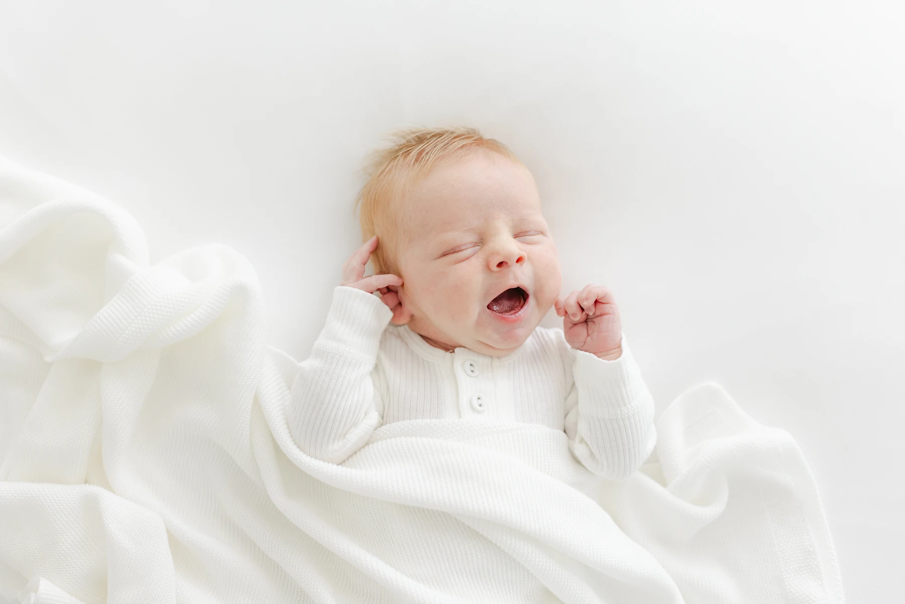 Sleeping newborn tucked into soft white blankets at an Omaha newborn photography session